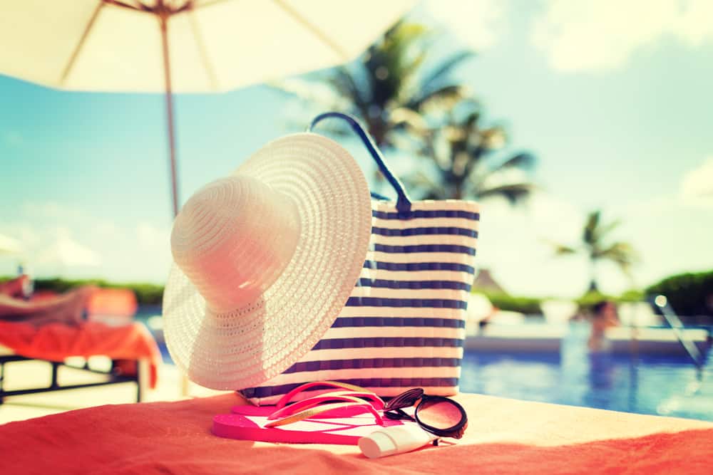 Hat, sunglasses and sunscreen on table by pool